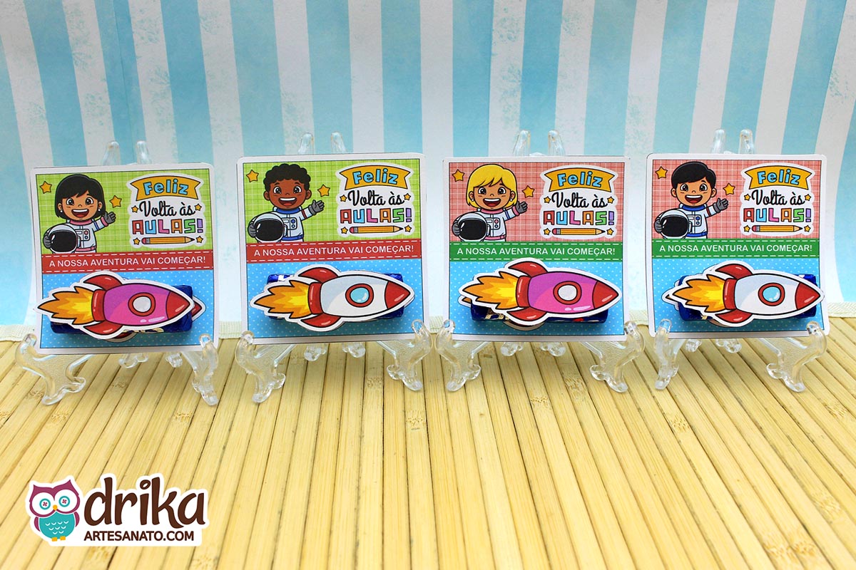 Quatro cartões porta-bis de astronautas meninos (cabelo crespo, loiro, liso) em suportes, com foguetes 3D e a frase "Feliz Volta às Aulas"