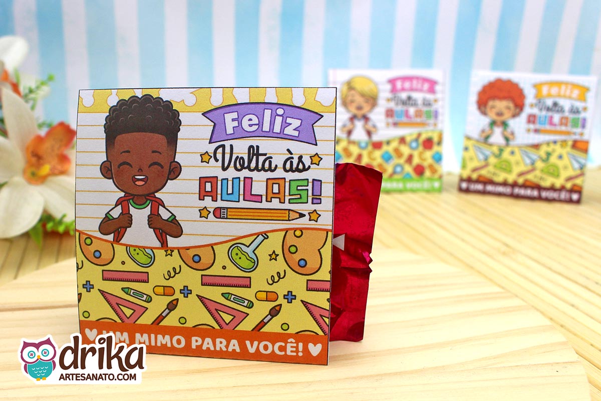 Porta-bombom de papel com menino de cabelo crespo sorridente e mochila, em fundo de caderno. Decorado com tubos de ensaio e pincéis