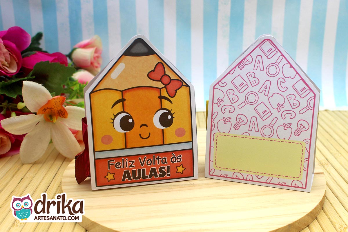 Porta-bombom lápis com rosto de menina e laço vermelho na frente e o verso com estampa escolar e espaço para mensagem