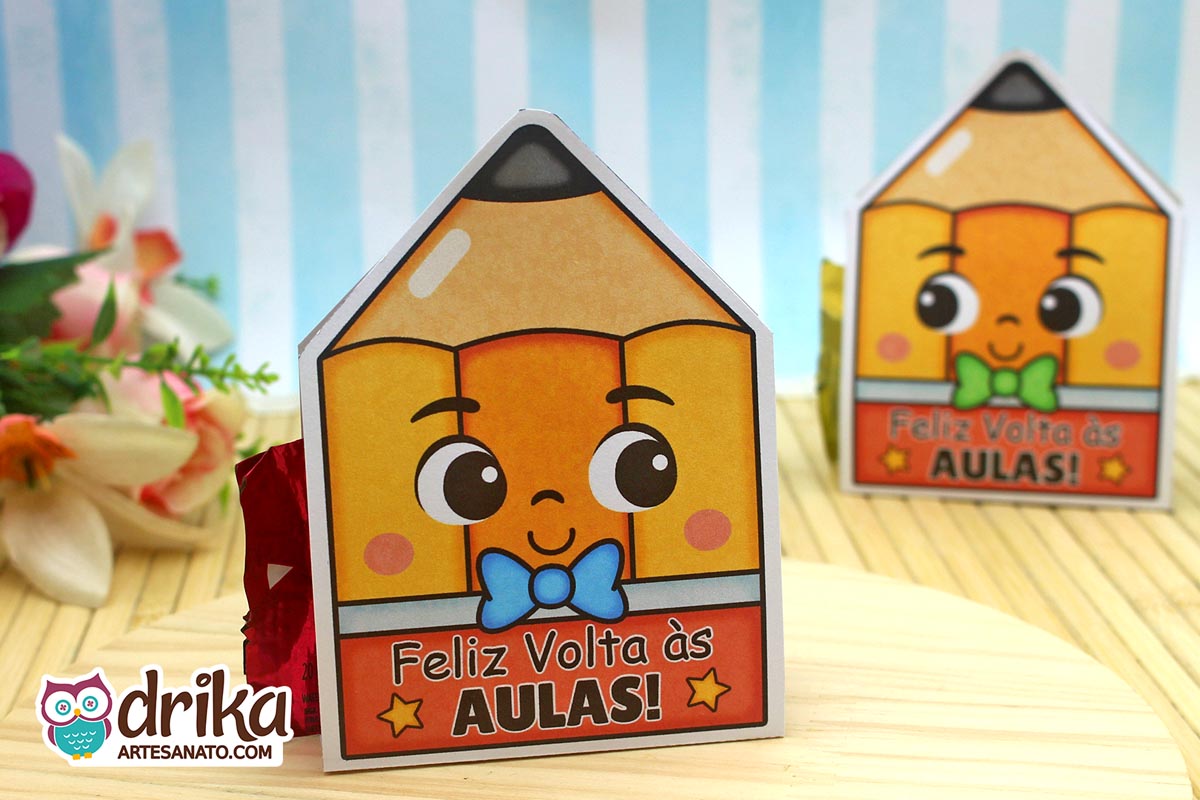 Porta-bombom de papel em formato de lápis amarelo com rosto fofo, gravatinha azul e a frase "Feliz Volta às Aulas"