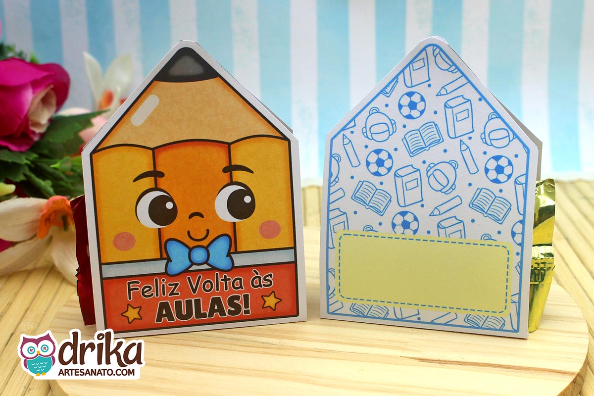 Porta-bombom lápis amarelo com rosto fofo e gravatinha azul ao lado do seu verso com estampa de material escolar e espaço para mensagem