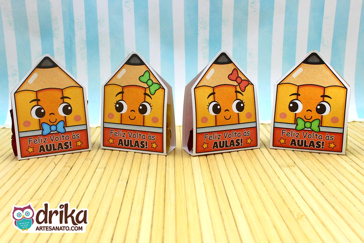Quatro porta-bombons de papel em formato de lápis com rostinhos fofos, com gravatinhas e lacinhos coloridos, e a frase "Feliz Volta às Aulas"