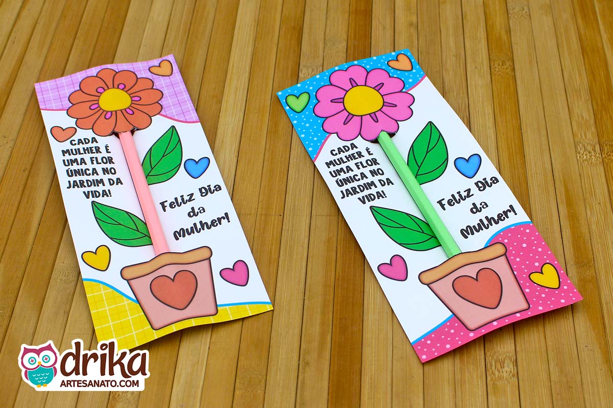 Dois cartões porta-lápis de papel com flores coloridas, lápis encaixados e frases de Dia da Mulher, sobre madeira