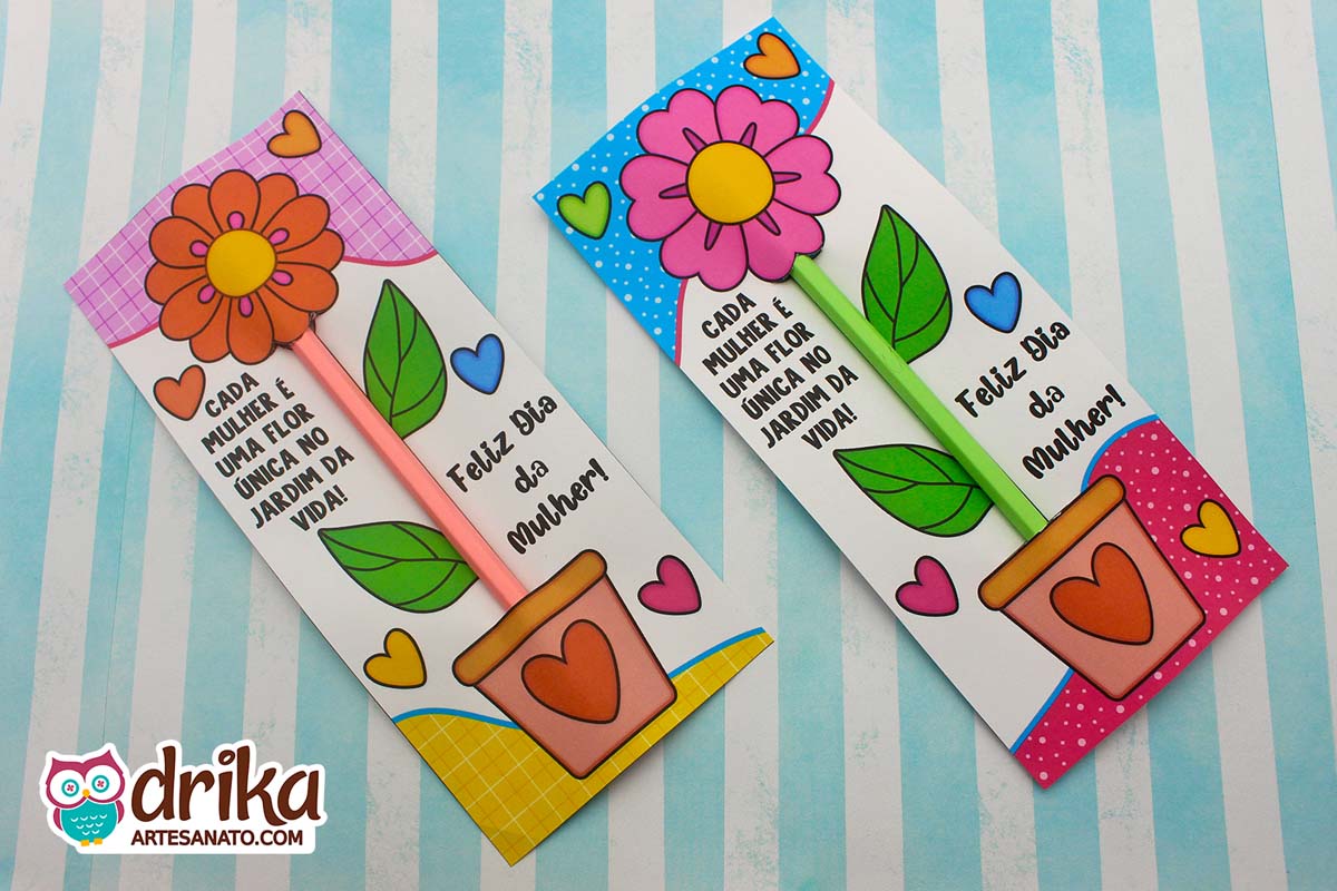 Dois cartões porta-lápis de papel com flores coloridas e lápis, sobre um fundo listrado azul e branco