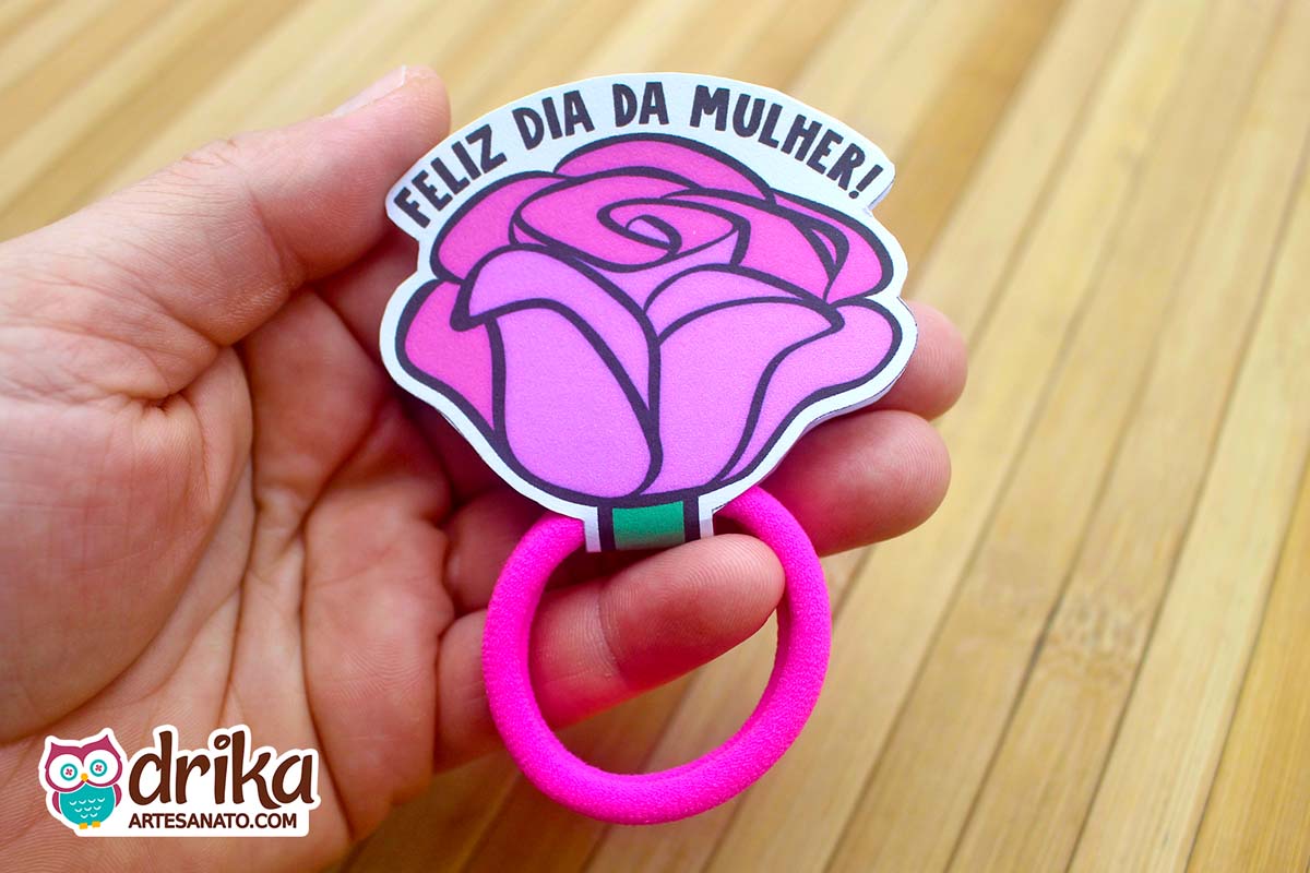 Mão segurando uma lembrancinha de rosa porta xuxinha de papel rosa vibrante com lacinho fúcsia