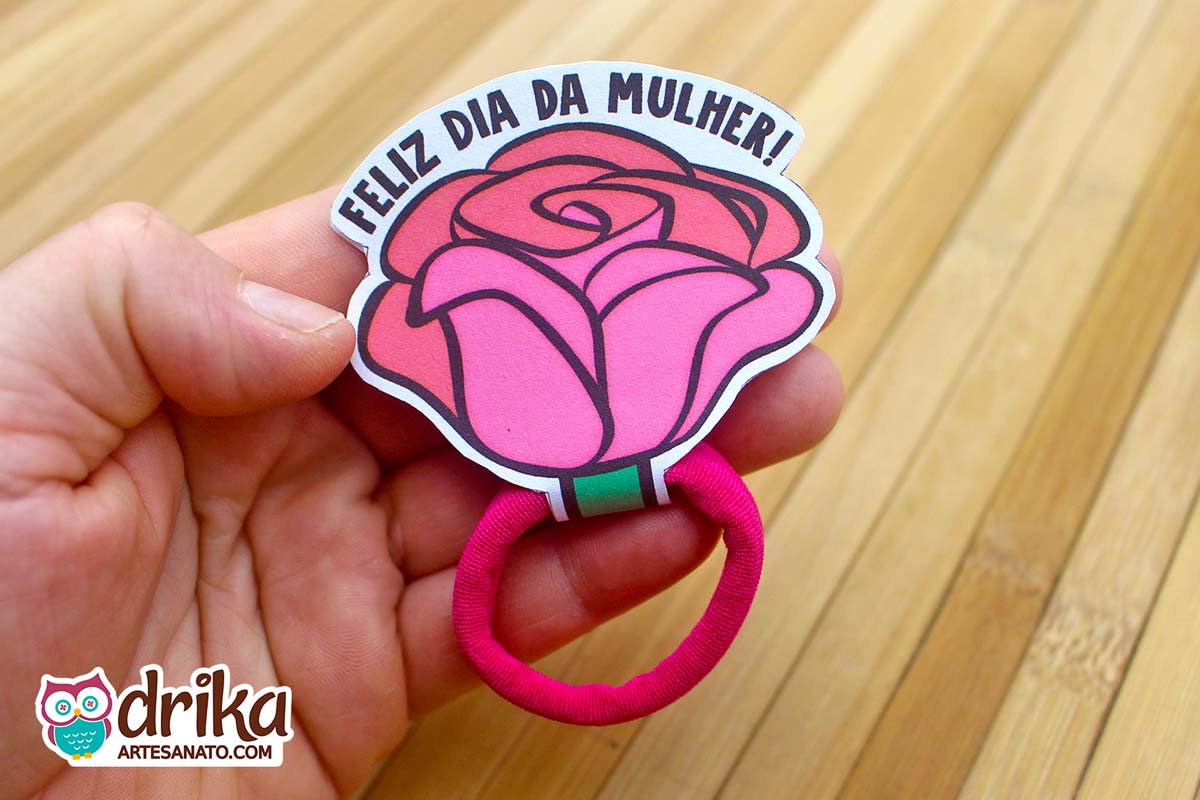 Mão segurando uma lembrancinha de rosa porta xuxinha de papel rosa suave com lacinho pink