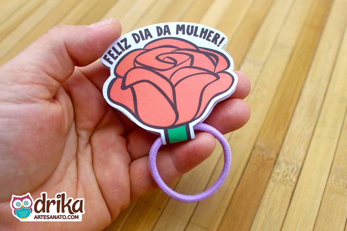 Mão segurando uma lembrancinha de rosa porta xuxinha de papel laranja com lacinho lilás