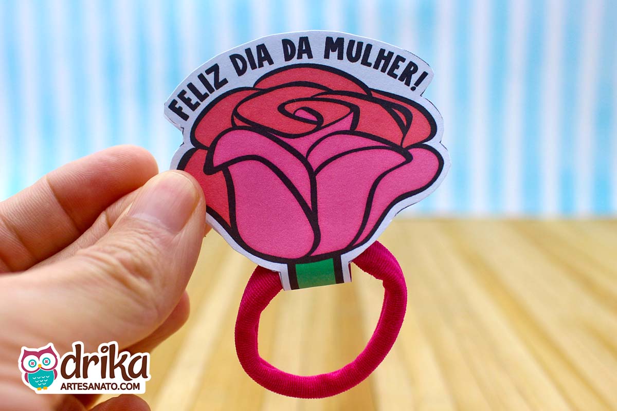 Mão segurando lembrancinha de Dia da Mulher em formato de rosa pink de papel com frase e xuxinha magenta