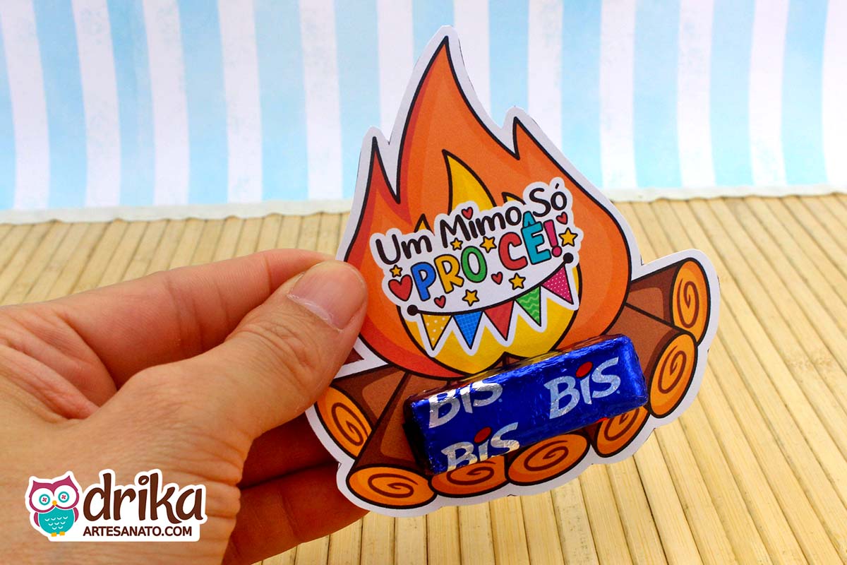 Mão segurando porta-bis de papel com desenho de fogueira e um chocolate Bis azul encaixado na base