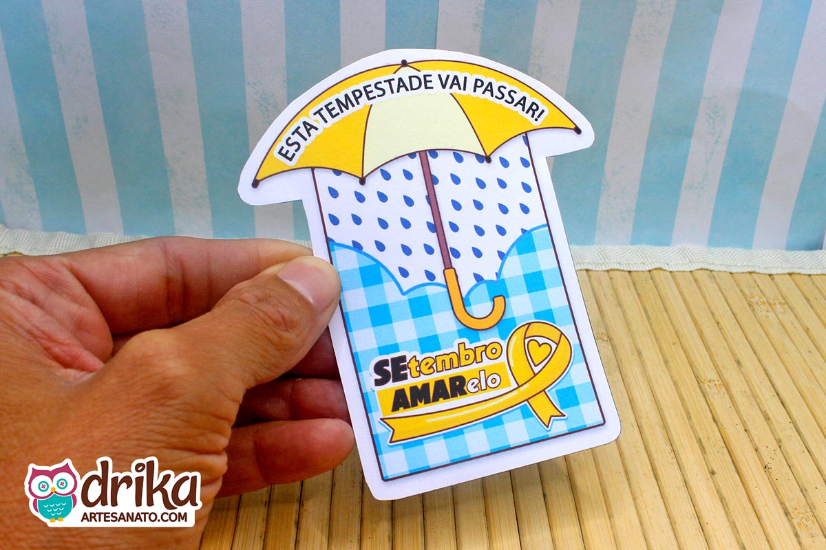 Mão segurando cartão de papel em formato de guarda-chuva com estampa de padrão xadrez azul