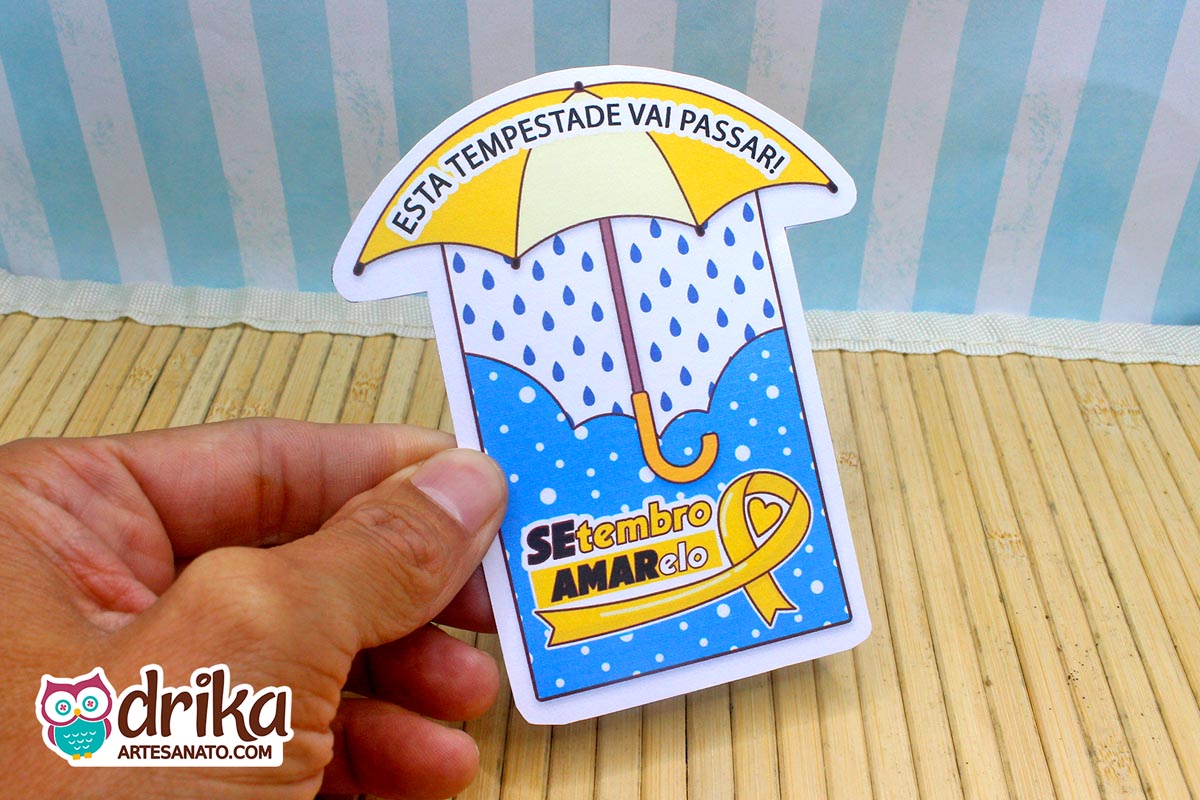 Mão segurando cartão de papel em formato de guarda-chuva com estampa de bolinhas brancas sobre fundo azul