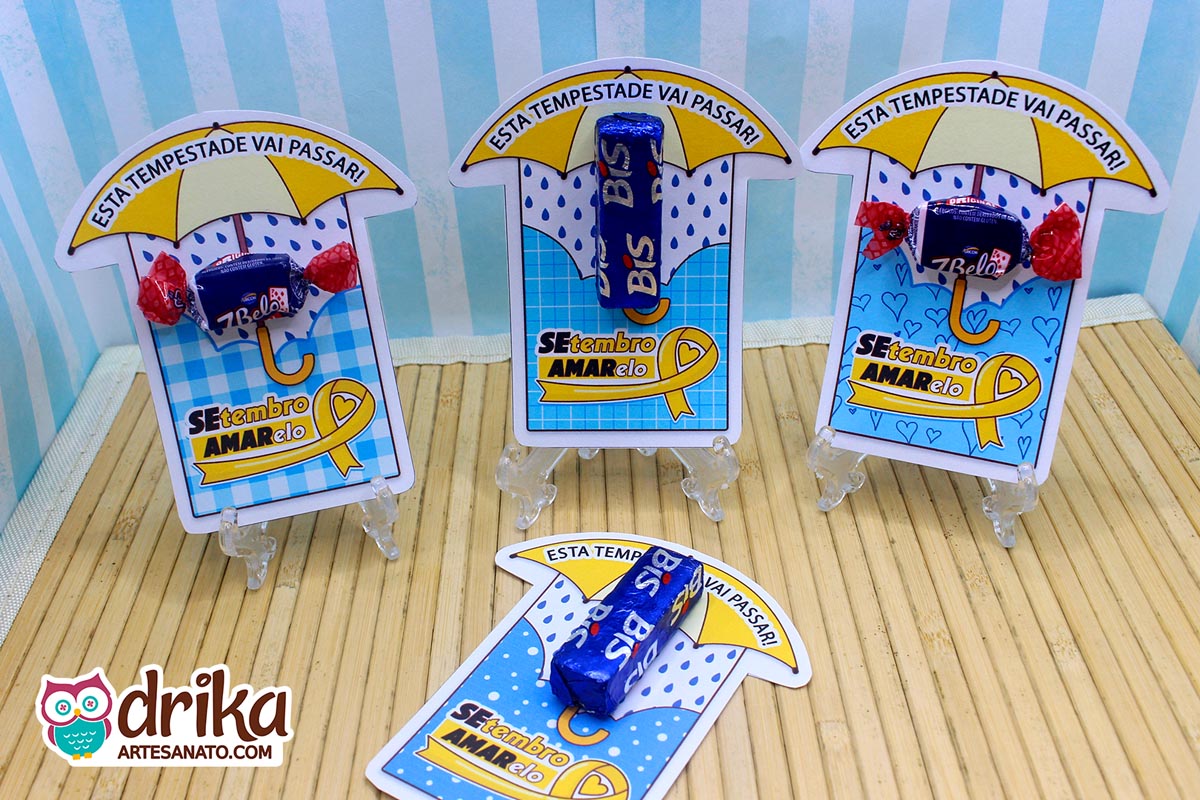 Três porta-bis em pé e um deitado, focando nos detalhes das estampas de guarda-chuva e laços amarelos